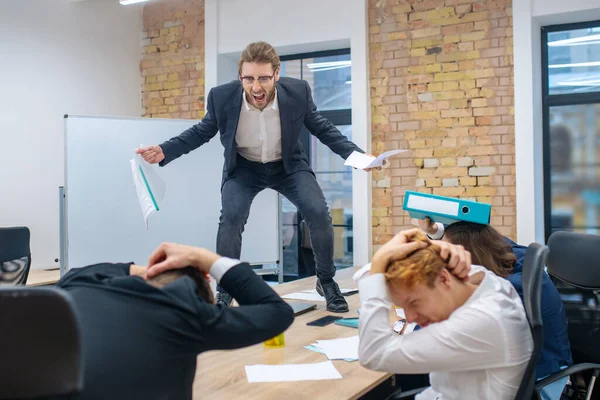 Arg man står på bordet och skrämda anställda — Stockfoto