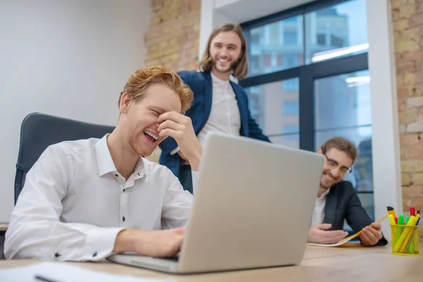 Man bakom laptop och kollegor roligt skrattar — Stockfoto