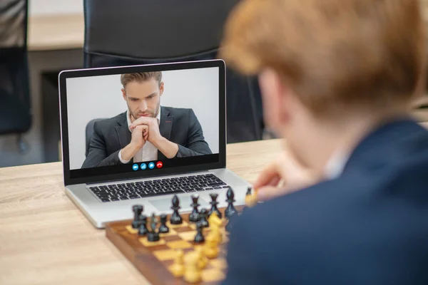 Man thinking over chess move in laptop screen