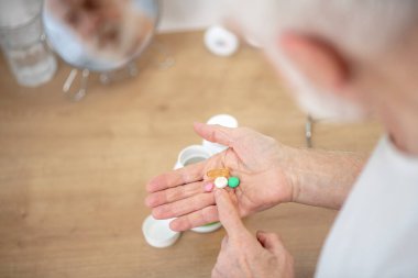 Beyaz tişörtlü, elinde vitaminler olan gri saçlı bir adam.