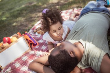 Afrikalı Amerikalı bir adam ve küçük kızı parkta dinleniyorlar.