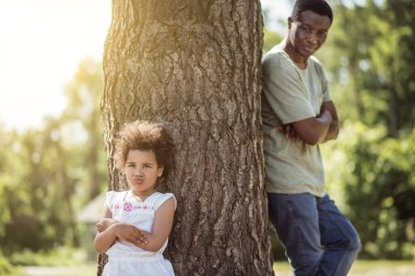 Kıvırcık saçlı küçük kız kollarını kavuşturmuş, gücenmiş görünüyor.