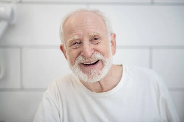 Homem de cabelos grisalhos em tshirt branca rindo vigorosamente — Fotografia de Stock