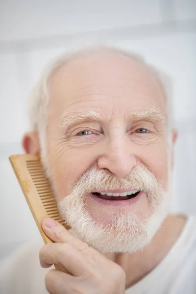 Close up of a gray-haired man brushing his beard — Stock Photo, Image