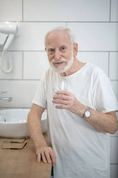 Ősz hajú férfi fehér pólóban a fürdőszobában. — Stock Fotó