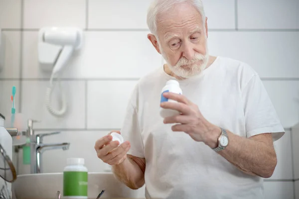 Šedovlasý muž v bílém tričku s lahvemi vitamínů v rukou — Stock fotografie