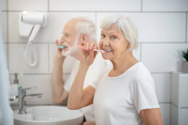 Yaşlı çift dişlerini birlikte fırçalıyorlar ve memnun görünüyorlar. — Stok fotoğraf