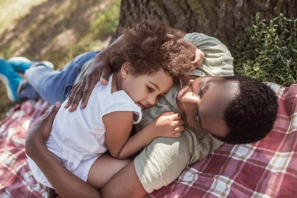 Hombre afroamericano abrazando a su linda hijita y descansando bajo el árbol —  Fotos de Stock