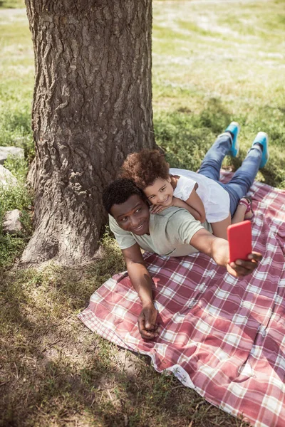 Hombre de piel oscura haciendo selfie con su hija pequeña en el parque —  Fotos de Stock