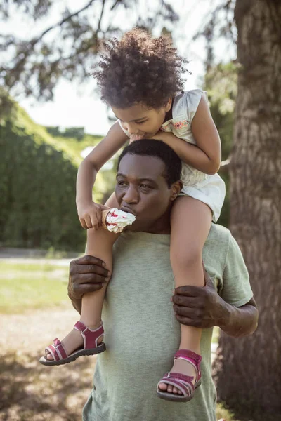 Niña linda de piel oscura sentada sobre los hombros de sus papás — Foto de Stock