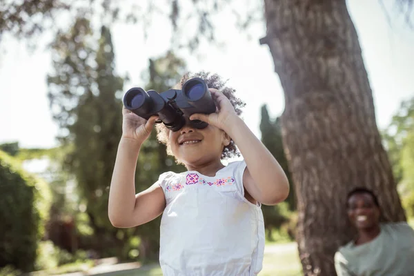 Fille mignonne à la peau foncée tenant une binoculaire et regardant intéressé — Photo