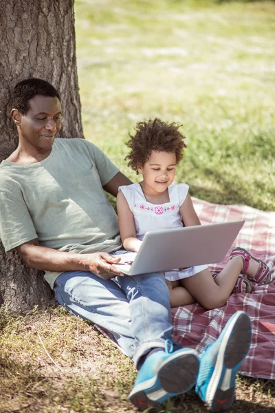Krullend klein meisje en haar vader kijken iets op laptop — Stockfoto