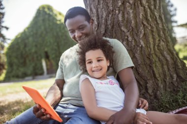 Afrikalı Amerikalı bir adam ve tatlı çocuğu parkta piknik yapıyor ve mutlu oluyorlar.