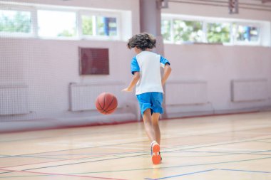 Spor giyim kuşağında siyah saçlı bir çocuk spor salonunda basketbol oynuyor.