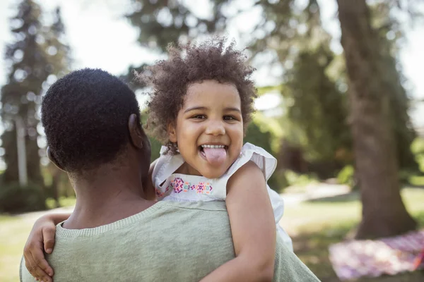 Niedliche lockige Kind sitzt spielen mit ihrem Vater und zeigt Zunge — Stockfoto