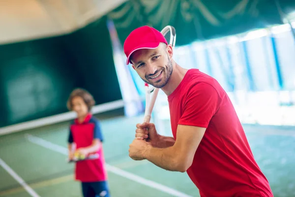 Junger bärtiger Mann mit roter Mütze schwenkt Tennisschläger — Stockfoto