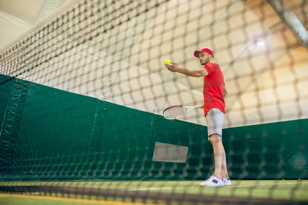 Jonge man met baard in een rode pet klaar om de tennisbal te raken — Stockfoto