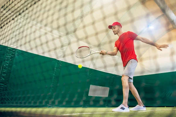 Jonge man met baard in een rode pet klaar om de tennisbal te raken — Stockfoto