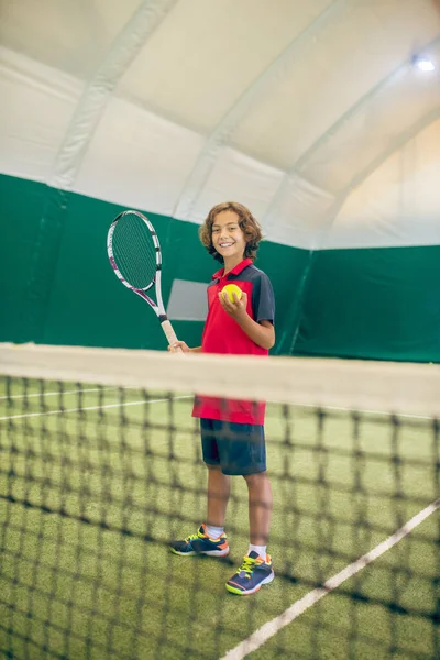 Темноволосый мальчик в красной футболке готов ударить по теннисному мячу. — стоковое фото
