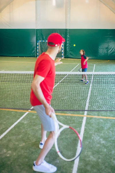 Trainer in roter Kleidung und Mütze spielt Tennis mit einem Jungen — Stockfoto