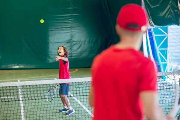 Trener w czerwonych ubraniach i czapce gra w tenisa z chłopcem — Zdjęcie stockowe
