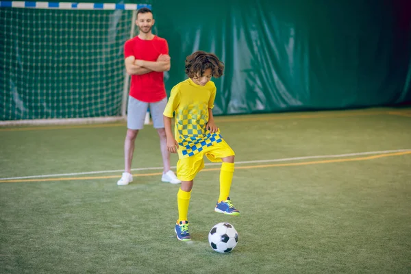 Escolar en uniforme amarillo jugando fútbol, su entrenador mirándolo — Foto de Stock