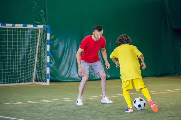 Niño en uniforme amarillo jugando al fútbol con su entrenador y buscando involucrado — Foto de Stock
