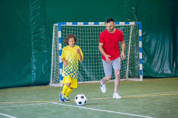 Niño en uniforme amarillo jugando al fútbol con su entrenador y buscando involucrado — Foto de Stock