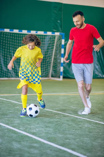 Niño en uniforme amarillo jugando al fútbol con su entrenador — Foto de Stock