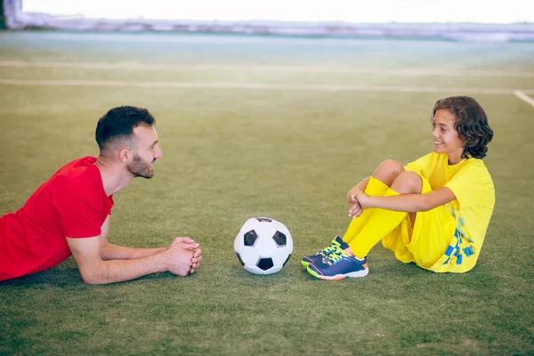 Menino de uniforme amarelo descansando após o jogo e conversando com seu treinador — Fotografia de Stock