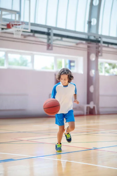 Chico en ropa deportiva corriendo tras la pelota en un gimnasio — Foto de Stock