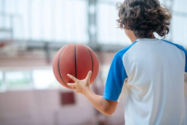 Donkerharige jongen in sportkleding playng basketbal in een sportschool — Stockfoto