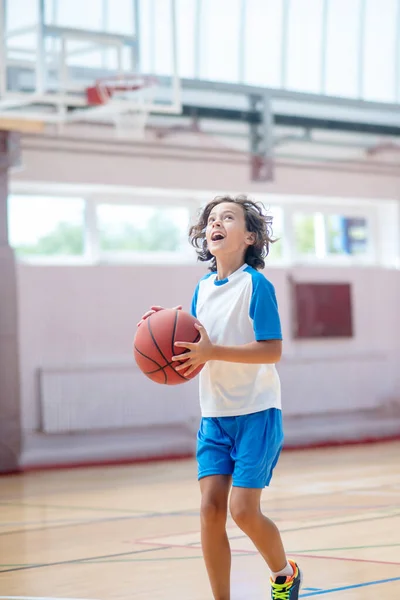 Garçon brun en tenue de sport prêt à lancer la balle dans le ring de basket — Photo