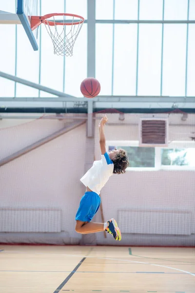 Ciemnowłosy chłopiec w sportowej odzieży gotowy rzucić piłkę na ring koszykówki — Zdjęcie stockowe