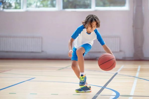 Donkerharige jongen in sportkleding traint zijn basketbal vaardigheden in een sportschool — Stockfoto