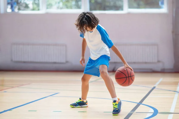 Écolier en vêtements de sport l'entraînement de ses compétences de basket-ball dans un gymnase — Photo