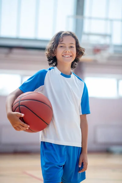 Menino de cabelos escuros em sportswear segurando uma bola e parecendo feliz — Fotografia de Stock