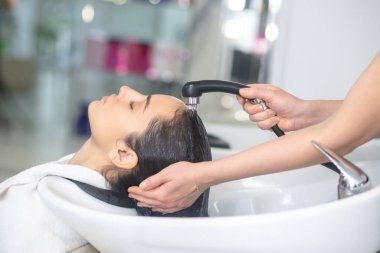 Saç stilisti saçını yıkarken kadın rahat görünüyor.