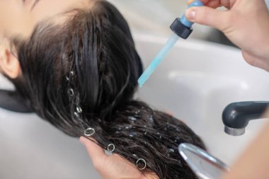 Saç stilisti müşterilerinin saçlarına serum sürüyor.