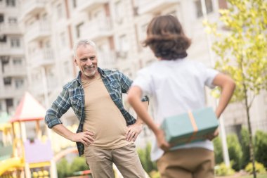 Çocuk hediye kutusunu tutarken baba düşünceli görünüyor.
