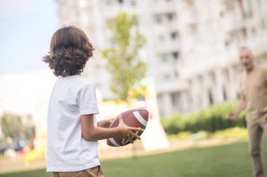 Siyah saçlı çocuk babasıyla top oynuyor.