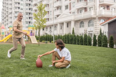 Siyah saçlı, beyaz tişörtlü, futbol oynayan çocuk.