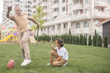 Siyah saçlı, beyaz tişörtlü, futbol oynayan çocuk.