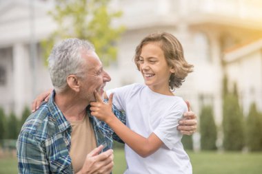 Gri saçlı adam oğluna sarılıyor ve mutlu görünüyor.