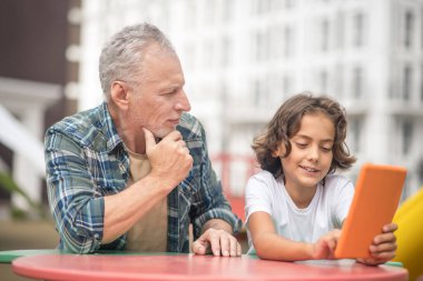 Oğlu ve babası tabletten bir şey izliyor ve düşünceli görünüyorlar.