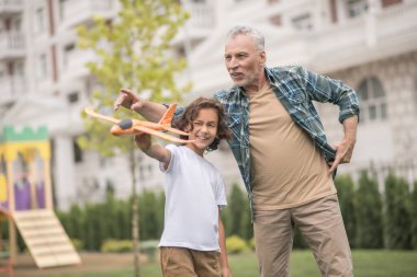 Koyu renk saçlı şirin bir çocuk babasıyla oyuncak uçak oynuyor ve mutlu.