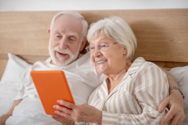 Yaşlı evli çift yatakta uzanıyor ve kitap okurken iyi vakit geçiriyor.