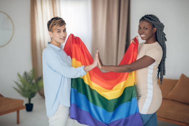 Gökkuşağı bayrağı taşıyan iki genç kız ve mutlu görünüyorlar.