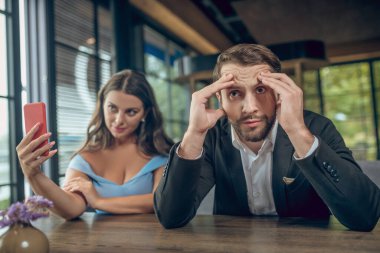 Selfie çeken bir kadın ve canı sıkkın bir adam.