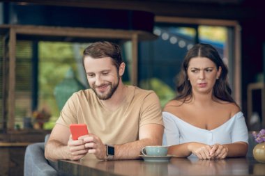 Akıllı telefonu ve kızgın kadını olan gülümseyen bir adam.